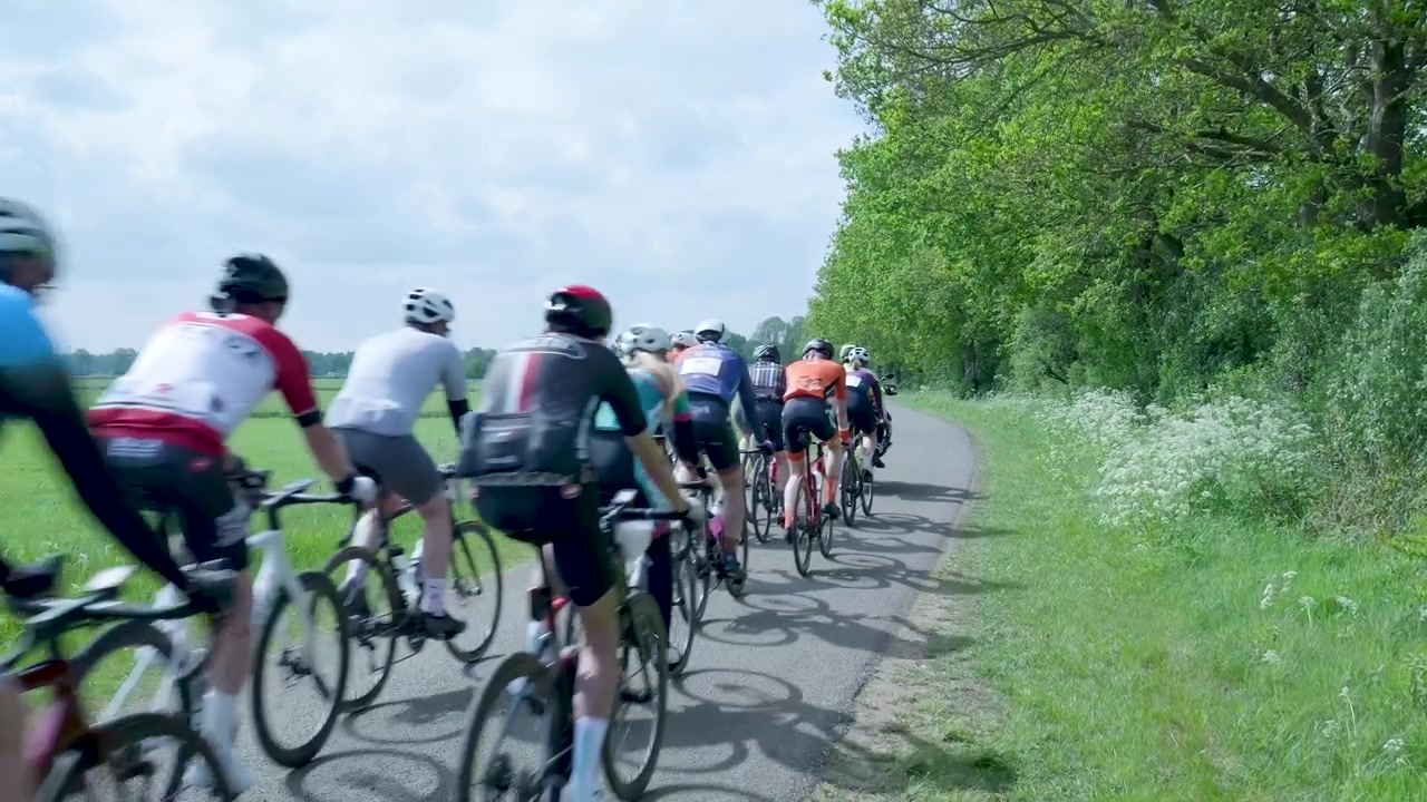 Grupo de ciclistas circulando por una carretera rural seguidos por una motocicleta