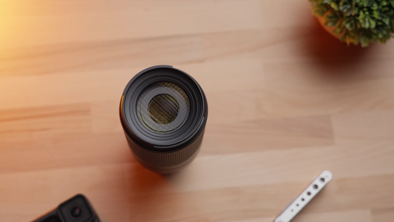 Camera lens and action camera on a wooden desk lit by warm sunlight