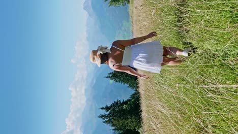 vertical shot of cute woman walking through green grass on hill in austria during summer - following shot