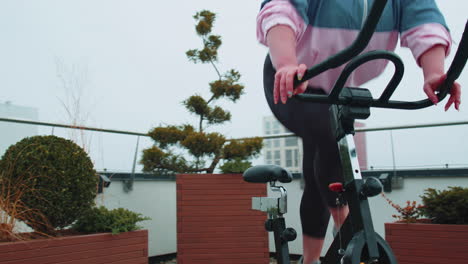 Athletic-woman-riding-on-spinning-stationary-bike-training-routine-on-house-rooftop,-weight-loss