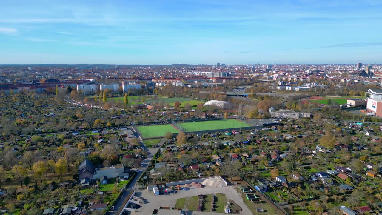 Berlin urban landscape with a large allotment garden area, sports soccer fields, football pitches and city infrastructure. Unique aerial view flight ascending raise up drone