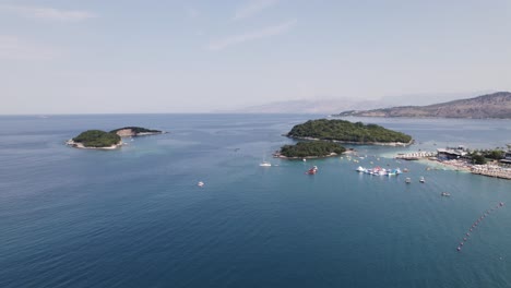 Toma-Aérea-De-La-Playa-Y-Las-Islas-Rodeadas-De-Barcos-Y-Yates-En-Ksamil,-Albania