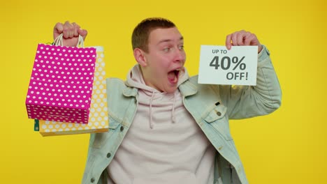 cheerful teen man showing shopping bags and up to 40 percent off inscriptions banner, black friday