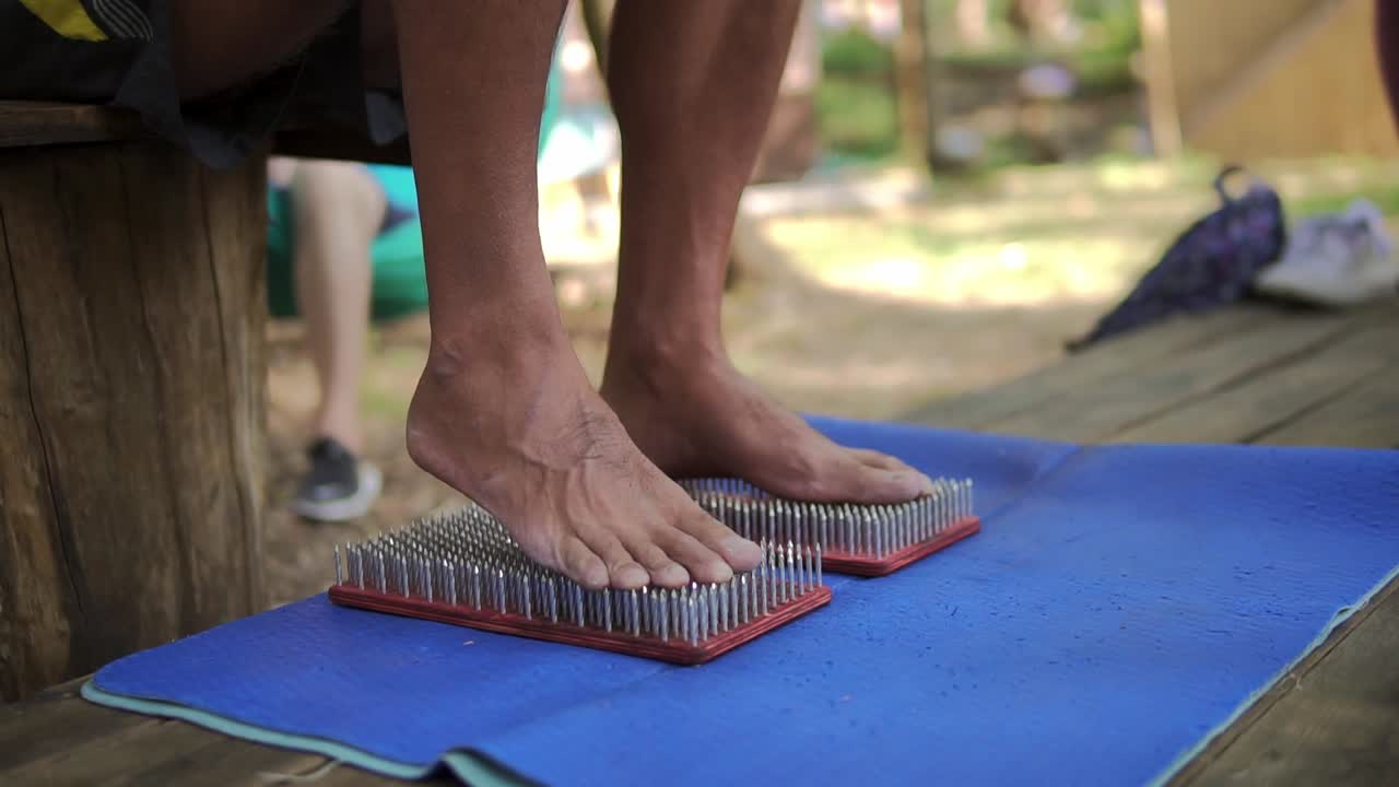 Piedi maschili poggiano su una tavola da yoga di legno con molti chiodi di metallo, poi ne escono con cautela
