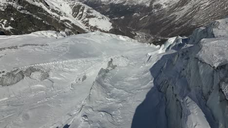 Vista-Aérea-De-Una-Fachada-Montañosa-En-Los-Alpes:-Glaciar-Con-Relieve-Y-Valle-Cuesta-Abajo