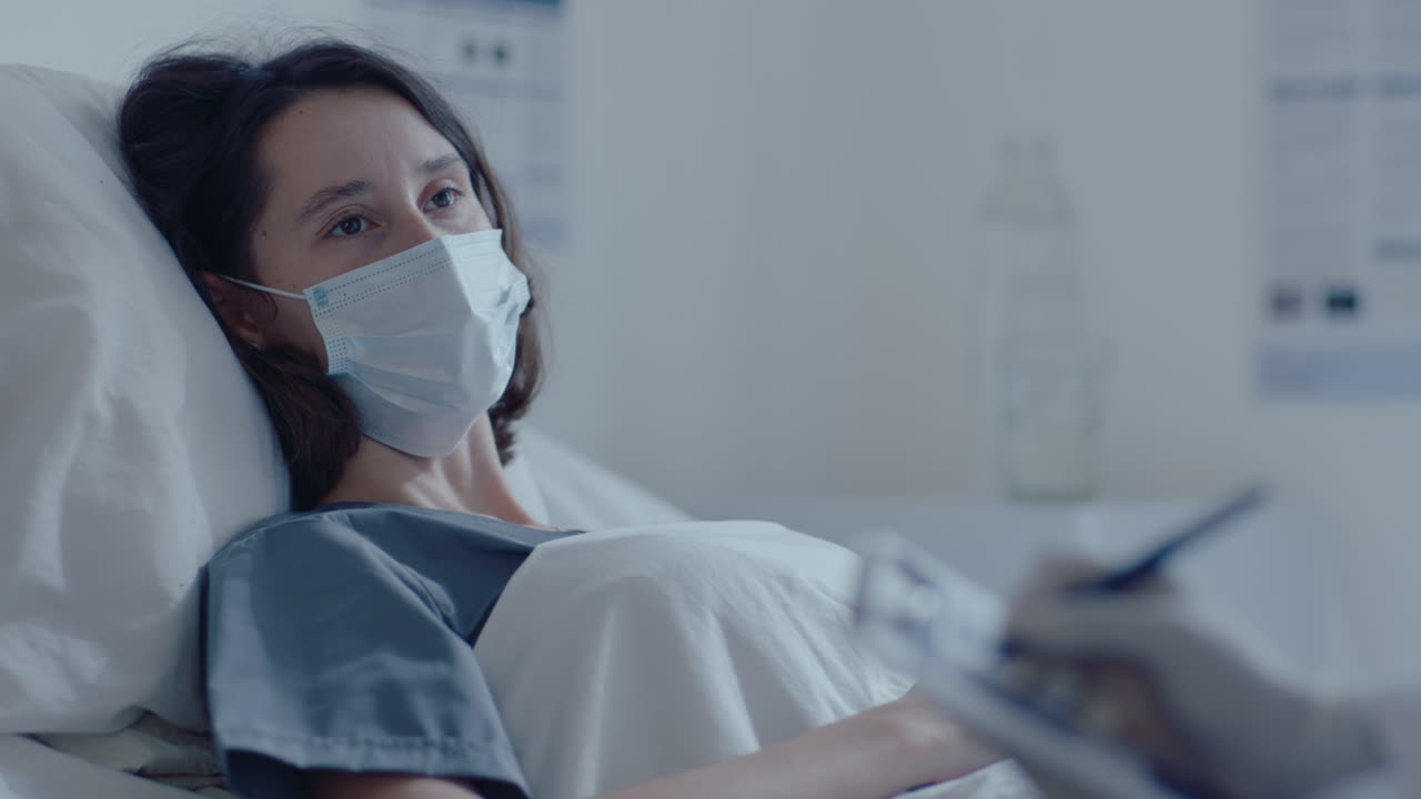 얼굴 마스크를 입은 여성 환자가 병원 병실에서 의사와 이야기하고 있습니다.