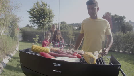 man standing at barbecue grill watching meat and vegetables