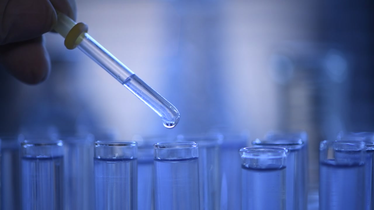 Primo piano di un contagocce che aggiunge liquido blu a una provetta in laboratorio