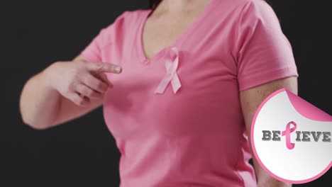 Believe-text-banner-against-mid-section-of-woman-wearing-pink-ribbon-on-her-chest