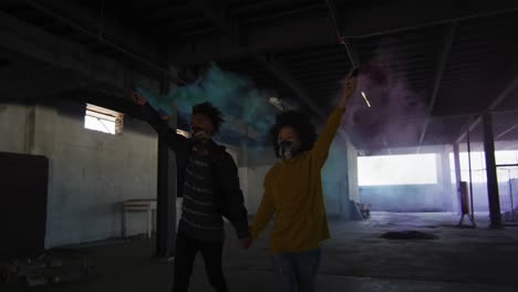 mixed race man and woman holding blue and purple flares walking through an empty building