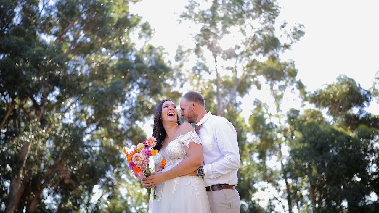 Toma de ángulo bajo de novios compartiendo una risa en un jardín soleado durante las fotos