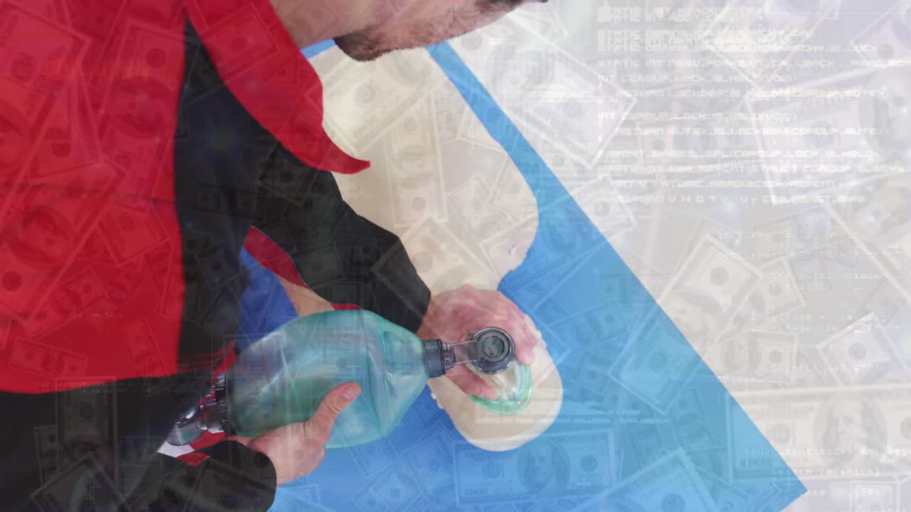 Animation of dollar bills and graphs over caucasian man using bag valve mask on cpr dummy