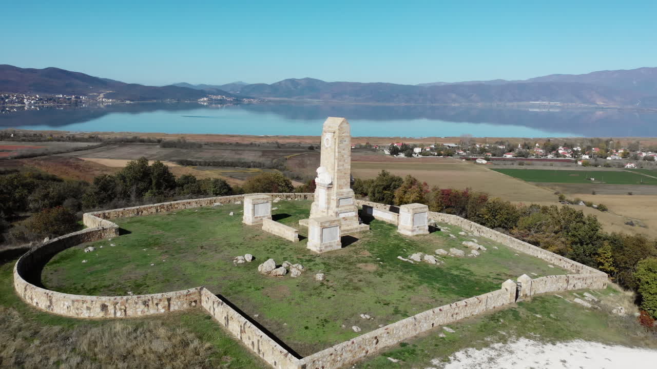 Riprese drone in una giornata di sole del Memoriale di Doiran e del Cimitero Militare che si affaccia sul Lago Doiran con una scultura di leone sulla sommità e un paesaggio montano rurale oltre.