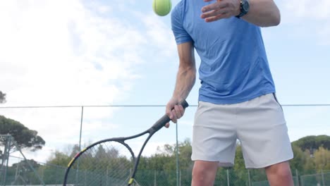 Midsection-of-caucasian-male-tennis-player-hitting-ball-with-racket-at-outdoor-court-in-slow-motion