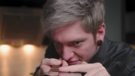 evil stare at chopping knife and camera while touching blade by young crazy psychopath male chef in elegant black shirt with an alternative look and tattoo modern, fancy looking kitchen slow mo dolly