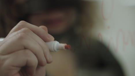 Close-up-of-girl's-hands-writing-on-transparent-glass-screen-with-red-marker,-slow-motion