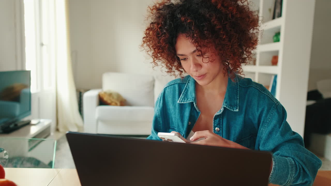 Ung kvinde, der bruger smartphone og laptop derhjemme