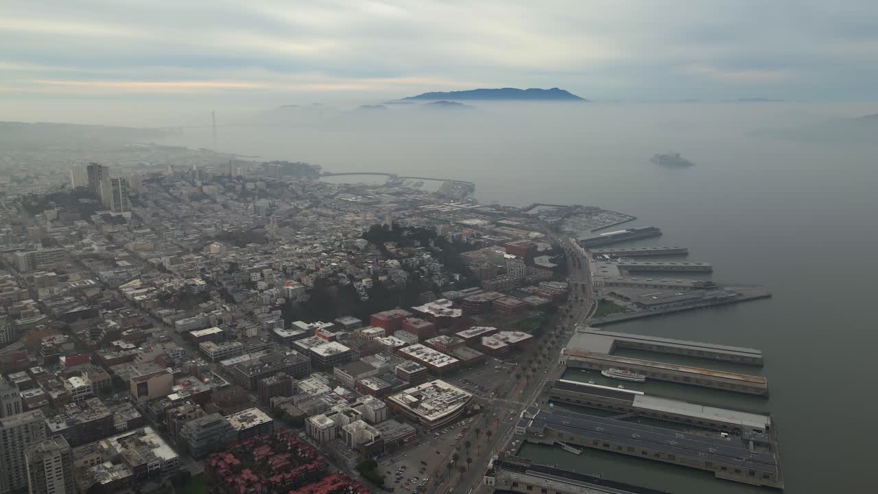 Aerial view of coastal piers and buildings, foggy evening in San Francisco, USA - pan, drone shot