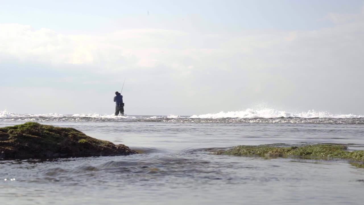 playa con mar agitado y muchas olas, con un pescador al fondo