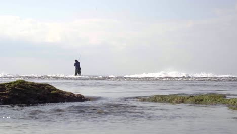 Beach-with-rough-sea-and-many-waves,-with-a-fisherman-in-the-background