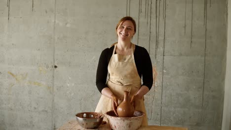 mujer alegre sosteniendo un jarrón de arcilla terminado y crudo. retrato de una alfarera, trabaja en un taller de cerámica con arcilla. el concepto de maestría y creatividad de la cerámica