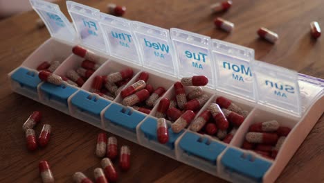 pills falling on a weekly medication organizer container in slow motion, and onto a wood kitchen table