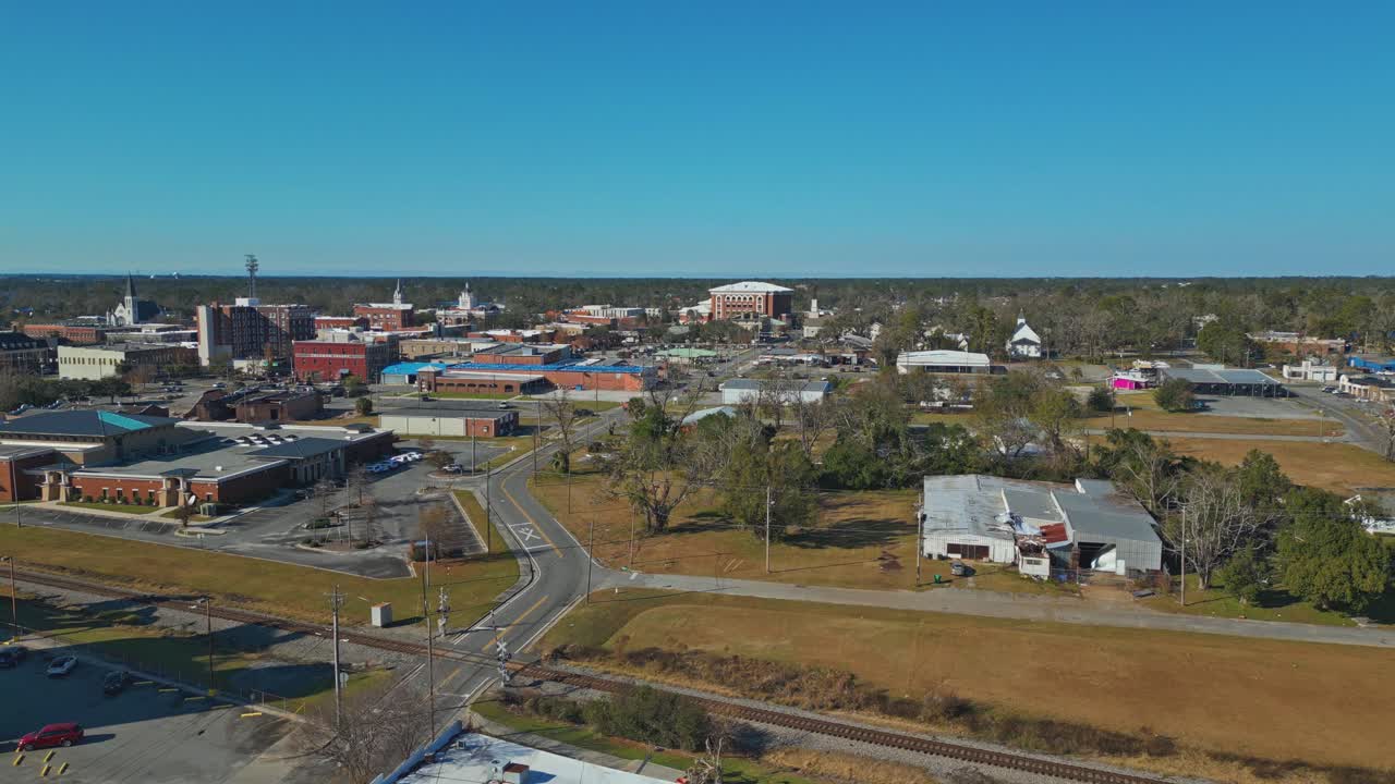 An Urban Area Features Church Steeples, Commercial Buildings, and Open Fields Under a Clear Blue Sky - Aerial Drone Shot