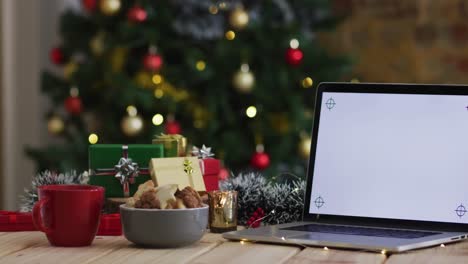 video of wooden table with christmas decorations and laptop with blank screen over christmas tree