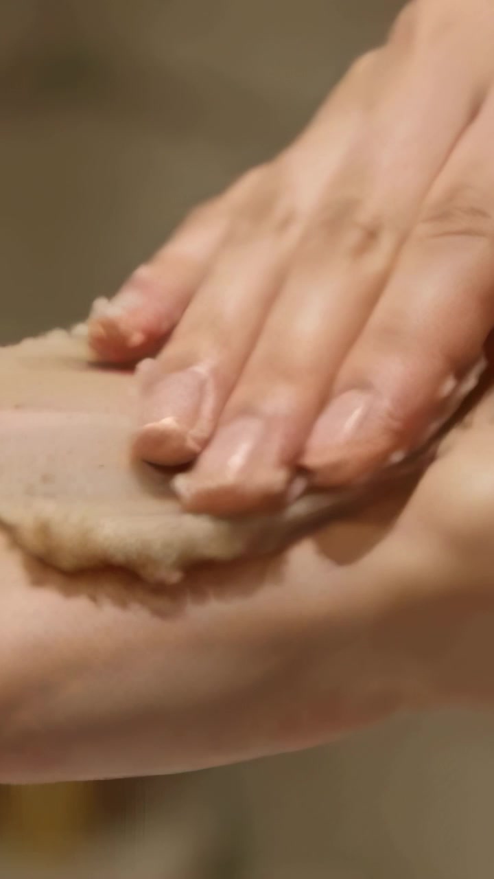 Video verticale: Mani che premono e strofinano un tampone esfoliante sull'avambraccio al lavandino per esfoliare.
