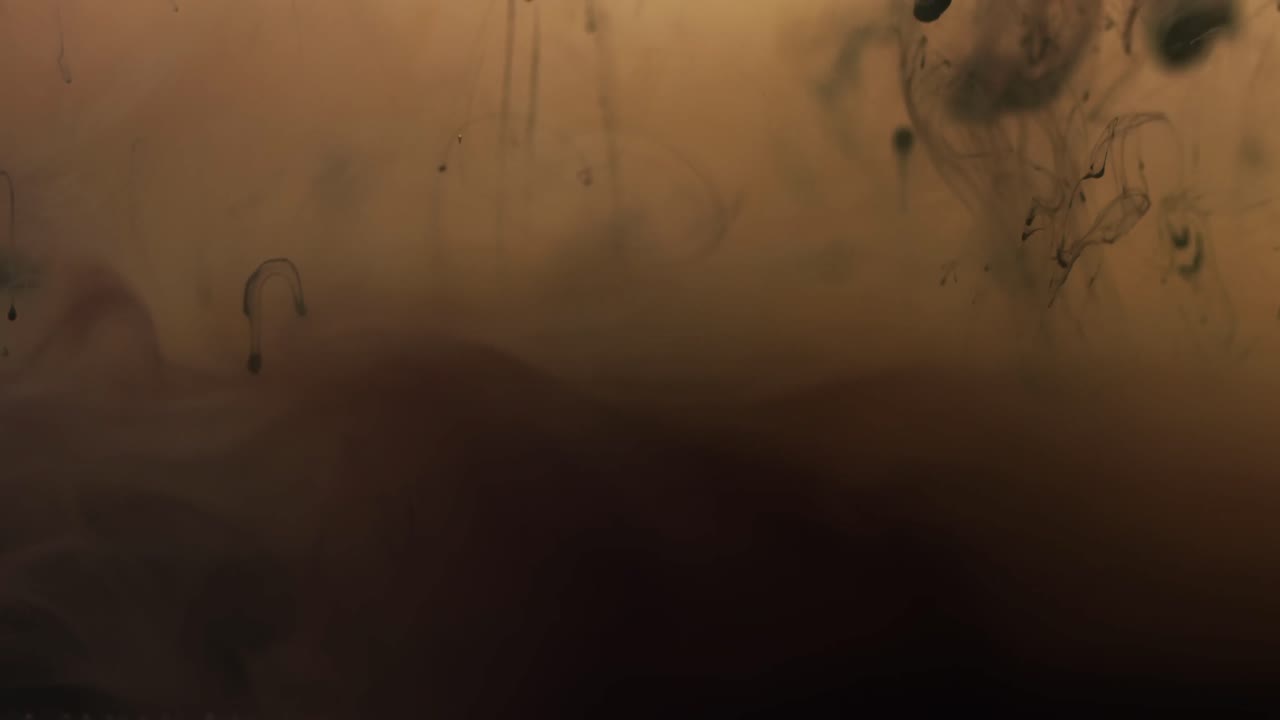 video en cámara lenta de tinta de acuarela negra mezclándose en agua contra un fondo marrón