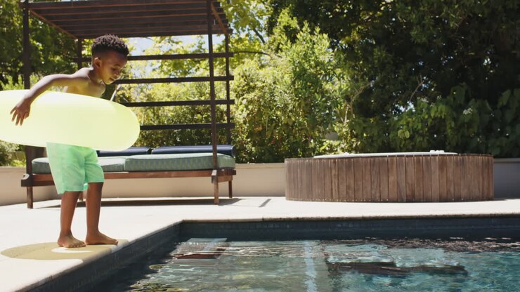 Happy african american boy jumping with inflatable at pool, in slow motion
