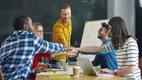 grupo de jóvenes empresarios multiculturales poniendo las manos encima de los demás y haciendo gestos de amistad, trabajo conjunto y solidaridad