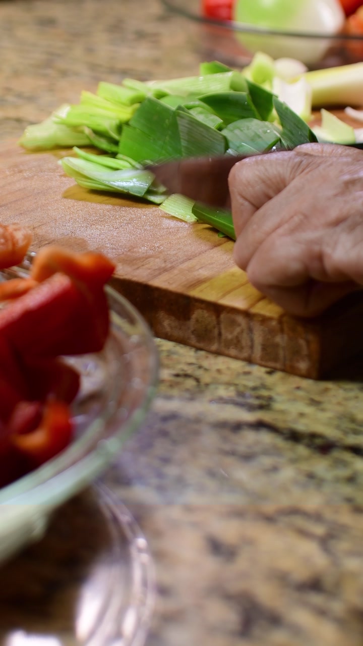 Vertical macro of hands cutting leeks on a rustic cutting board indoor