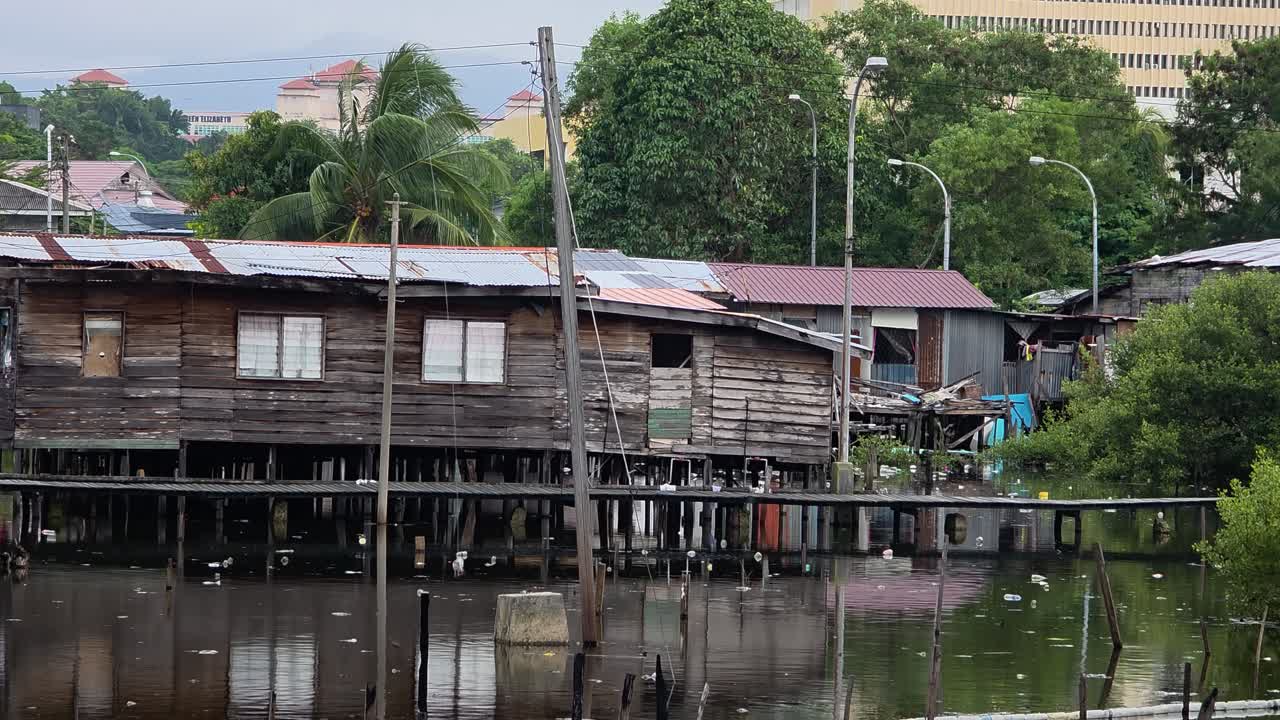 A view of a traditional water village in Kota Kinabalu, Malaysia, shows weathered wooden houses built on stilts over the water, reflecting a unique coastal lifestyle