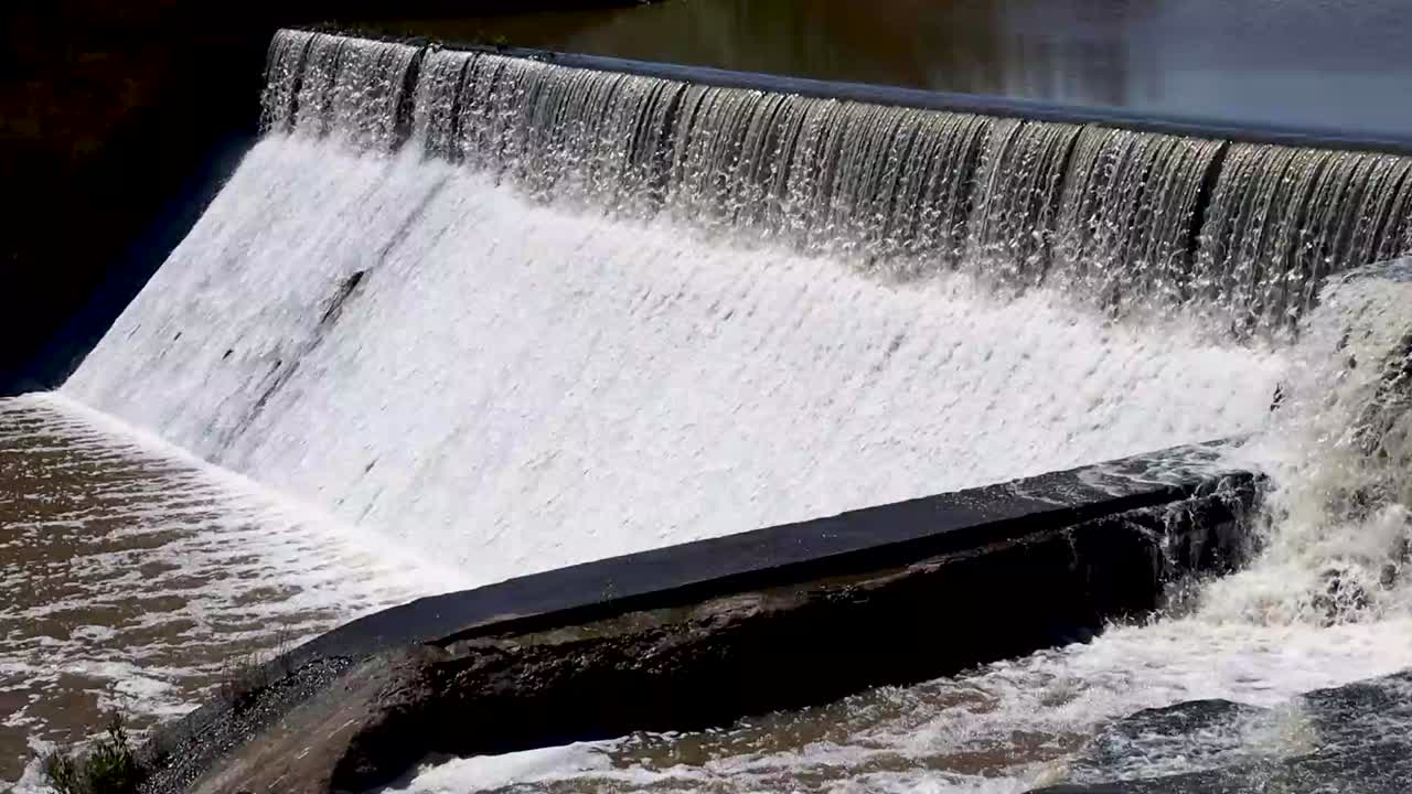 Dynamic close-up of water rushing over a small dam's spillway, capturing the power and flow. Perfect for nature, environment, and water management projects