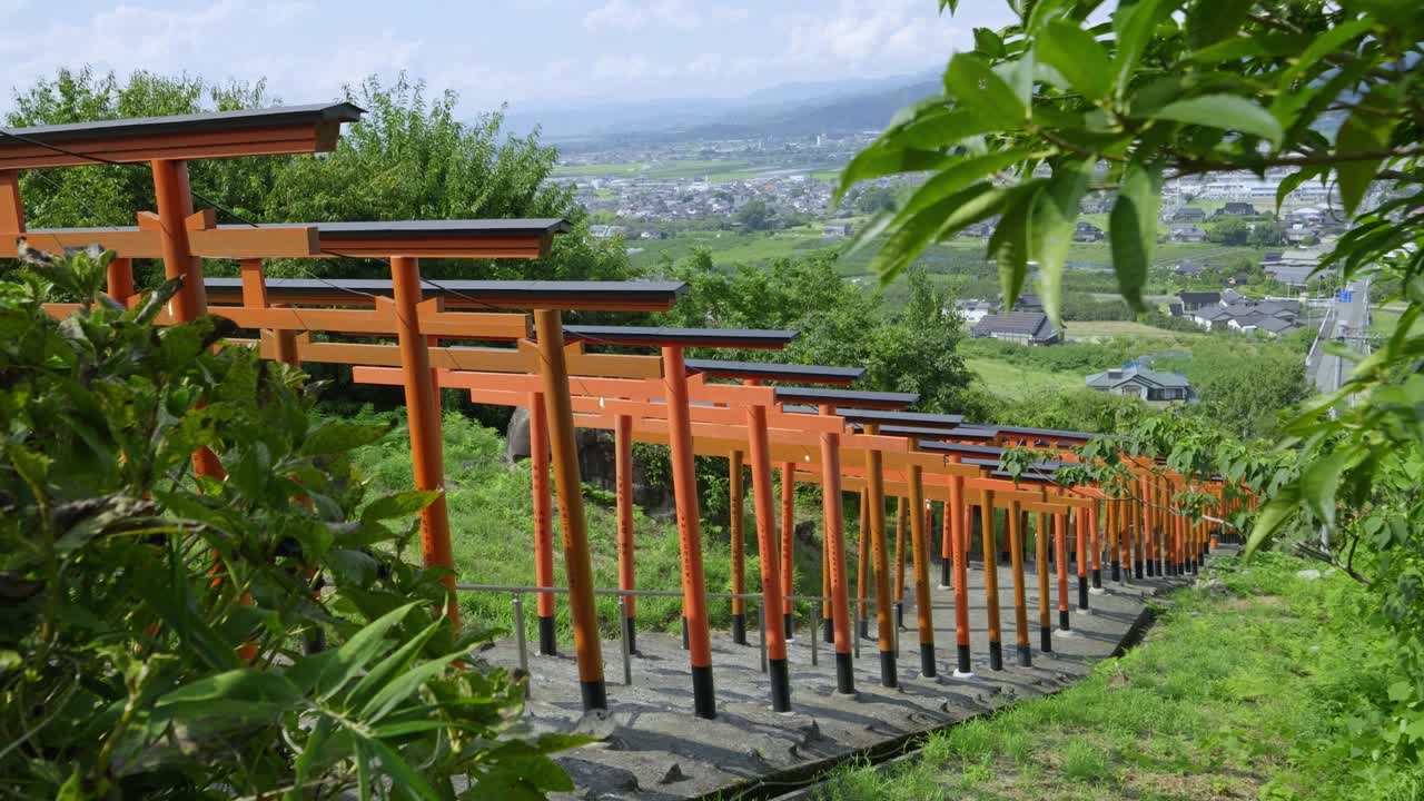 Sideways slider over rows of red Torii gates in Japanese countryside
