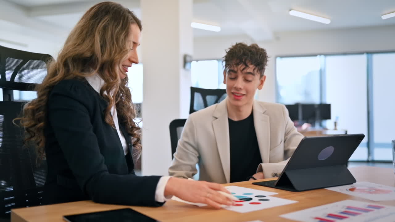 Business session in an office. Woman and a young man discussing business affairs. Gadgets with graphs and notes. Slow motion