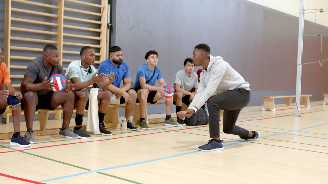 Ein Trainer spricht sein Volleyballteam an und demonstriert die Annahmestellung für das Training in der Sporthalle, mit Freiraum für Text.