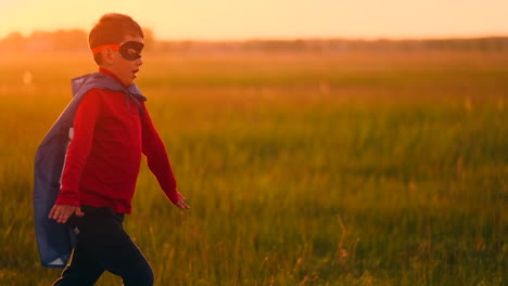 Ein-Junge-Im-Superheldenkostüm-Läuft-Bei-Sonnenuntergang-Lachend-Und-Lächelnd-über-Das-Feld.