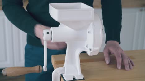 man assembles domestic flour mill at wooden table in kitchen