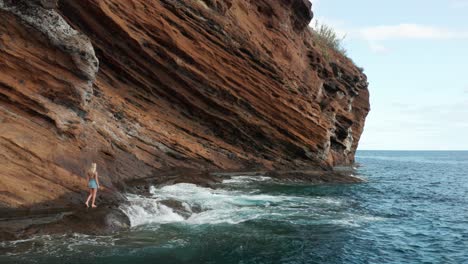 Adventure-girl-walks-on-slippery-pathway-at-rugged-cliffs-with-waves-of-Madeira