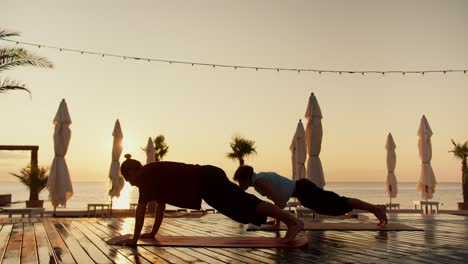 two guys doing wellness yoga on the beach at sunrise. sports and morning exercises