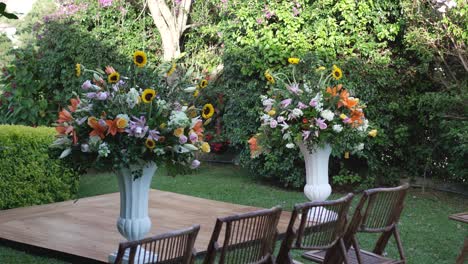 a beautiful garden with two vases of flowers with bamboo chairs around them, set for a wedding celebration