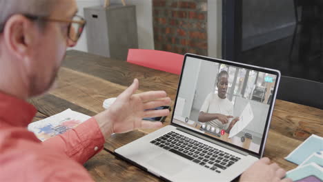 hombre de negocios caucásico en una llamada de video portátil con una colega afroamericana en la pantalla