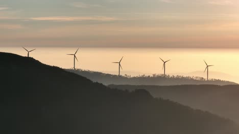 rotating wind power turbines on forest-covered hills at sunset in portugal