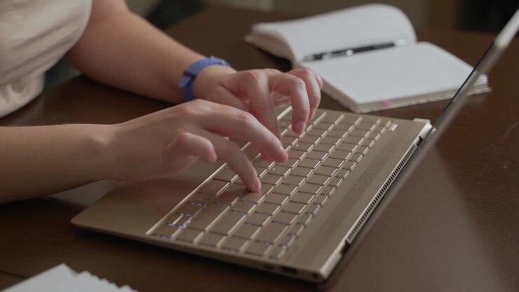 Female hands are typing text on laptop keyboard. Fingers quickly press the keys on the keyboard. There is notebook next to it. Personal computer, remote work at home, business, study, messaging, chat