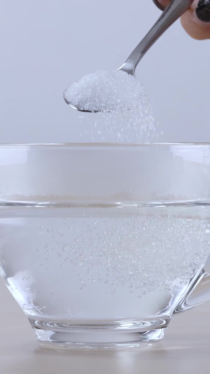 Zucchero granulato cade nell'acqua e viene mescolato con un cucchiaio di metallo in una tazza
