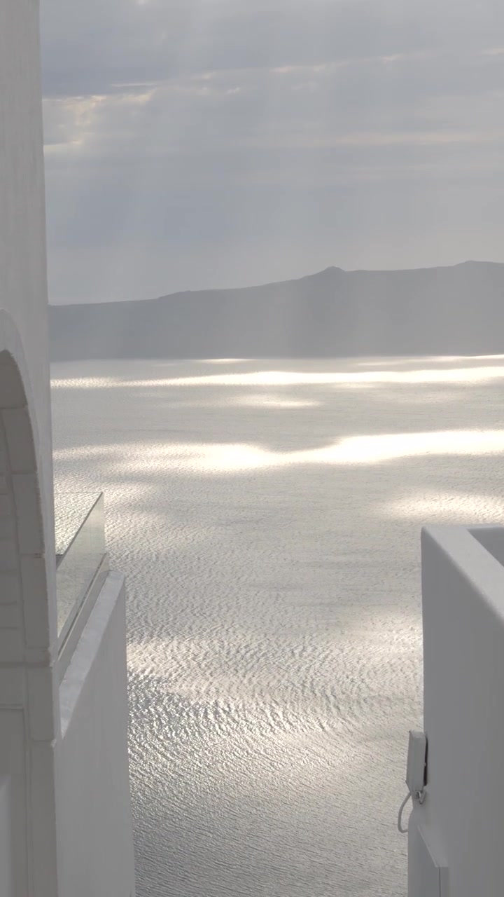 Vista verticale di un ingresso imbiancato a calce che incornicia una scintillante vista mare della caldera a Santorini, Grecia, mostrando una classica composizione incorniciata cicladica