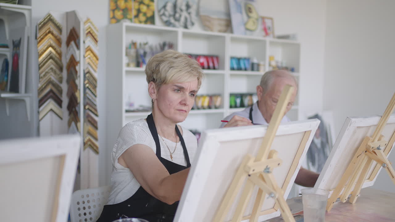 선생님 은 그림 을 그리는 수업 에서 은퇴 한 노인 들 의 친구 들 의 집단 을 보여 줍니다. 노인 남자 들 과 여자 들 의 집단 은 함께 그림 을 그리고 미소 짓습니다.