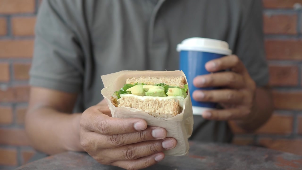 Person Holding Avocado Sandwich and Coffee Cup